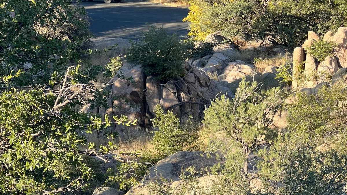 A tranquil outdoor scene showcasing Prescott’s iconic rock formations against a backdrop of green foliage, with a roadway suggesting access and adventure. The setting exudes calm and invites the viewer to imagine hiking or observing wildlife in the area.