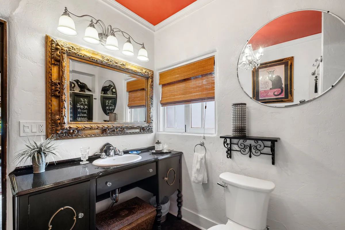 A modern bathroom with an ornate mirror, elegant light fixtures, a vanity with sink, and bamboo blinds. The space feels contemporary and inviting, ideal for relaxing self-care routines after an adventurous day.