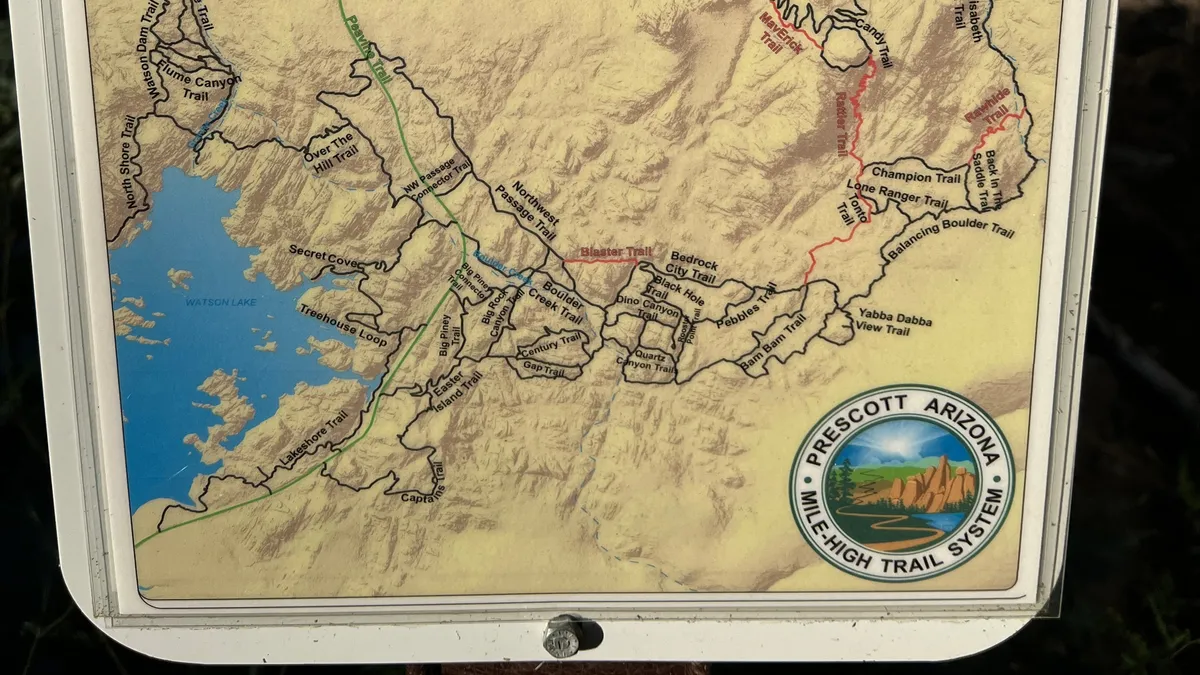 A vibrant exterior shot focused on a detailed trail map with the Mile High Trail System logo prominently displayed. The scene hints at the start of rugged trails, surrounded by natural landscape, ready for exploration on foot or bike.