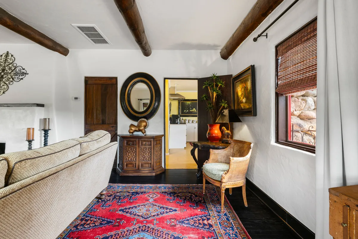 A comfortable and inviting living space featuring a plush sofa, decorative mirror, wooden cabinet, art piece, woven chair, and area rug. The arrangement encourages gatherings and provides quiet corners for reading or swapping stories.