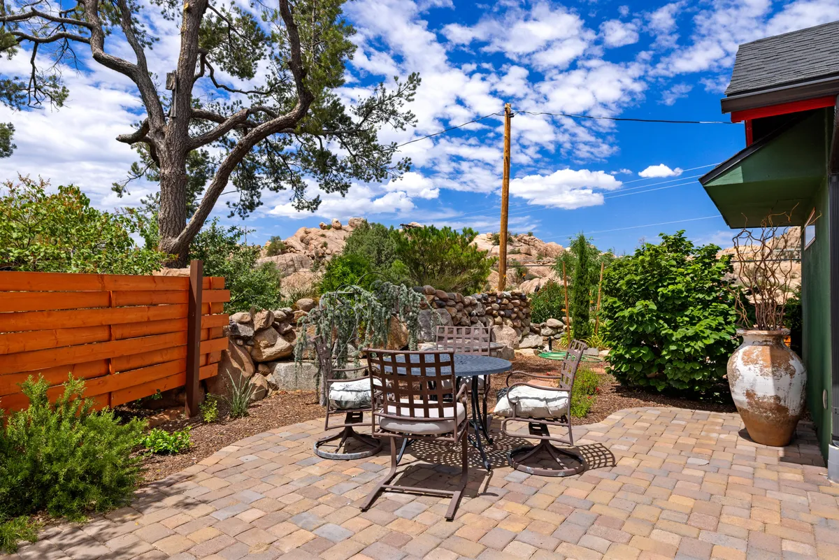 A serene outdoor dining area with a table and chairs set beside a stone wall, under the shade of a tree with a potted plant nearby. The mood is tranquil, suggesting moments of relaxation, alfresco meals, or evening stargazing after a day on the road.