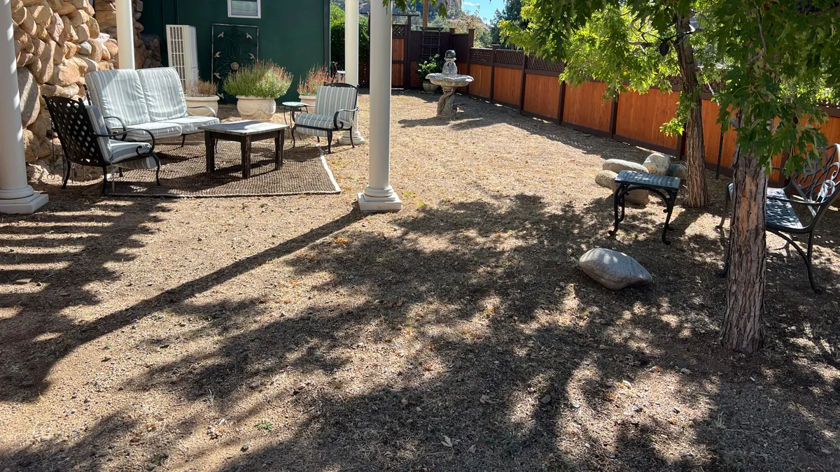 This exterior scene features a charming seating area surrounded by lush green foliage, with a tranquil fountain set against a rustic stone wall. The space invites relaxation, socializing, and immersion in nature, offering a gentle transition between indoor comfort and outdoor exploration.