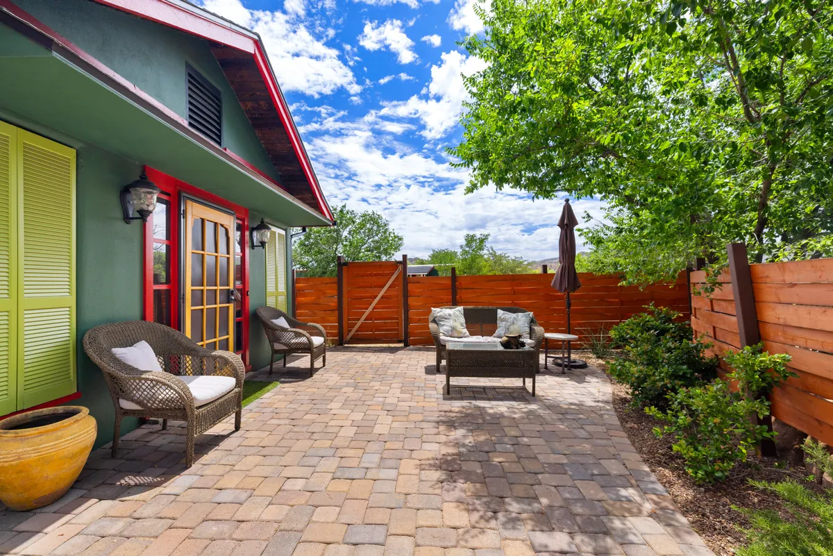 This image features a paved patio with inviting wicker chairs, green foliage, and the house’s colorful exterior in the background. The scene captures both social and serene moments, from sunny afternoons with friends to peaceful evenings under the patio umbrella.