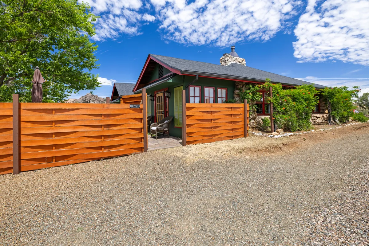 A welcoming exterior shot featuring a wooden gate, stone details, and green walls with red trim, surrounded by nature. The scene suggests an inviting transition from the comfort of home into the natural world beyond.