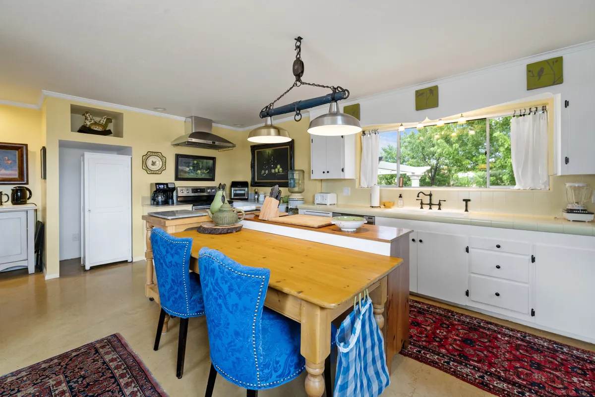 An inviting dining nook with a wooden table, blue upholstered chairs, and a large window that fills the space with natural light. A colorful rug adds warmth, making it ideal for both casual coffee or shared meals.